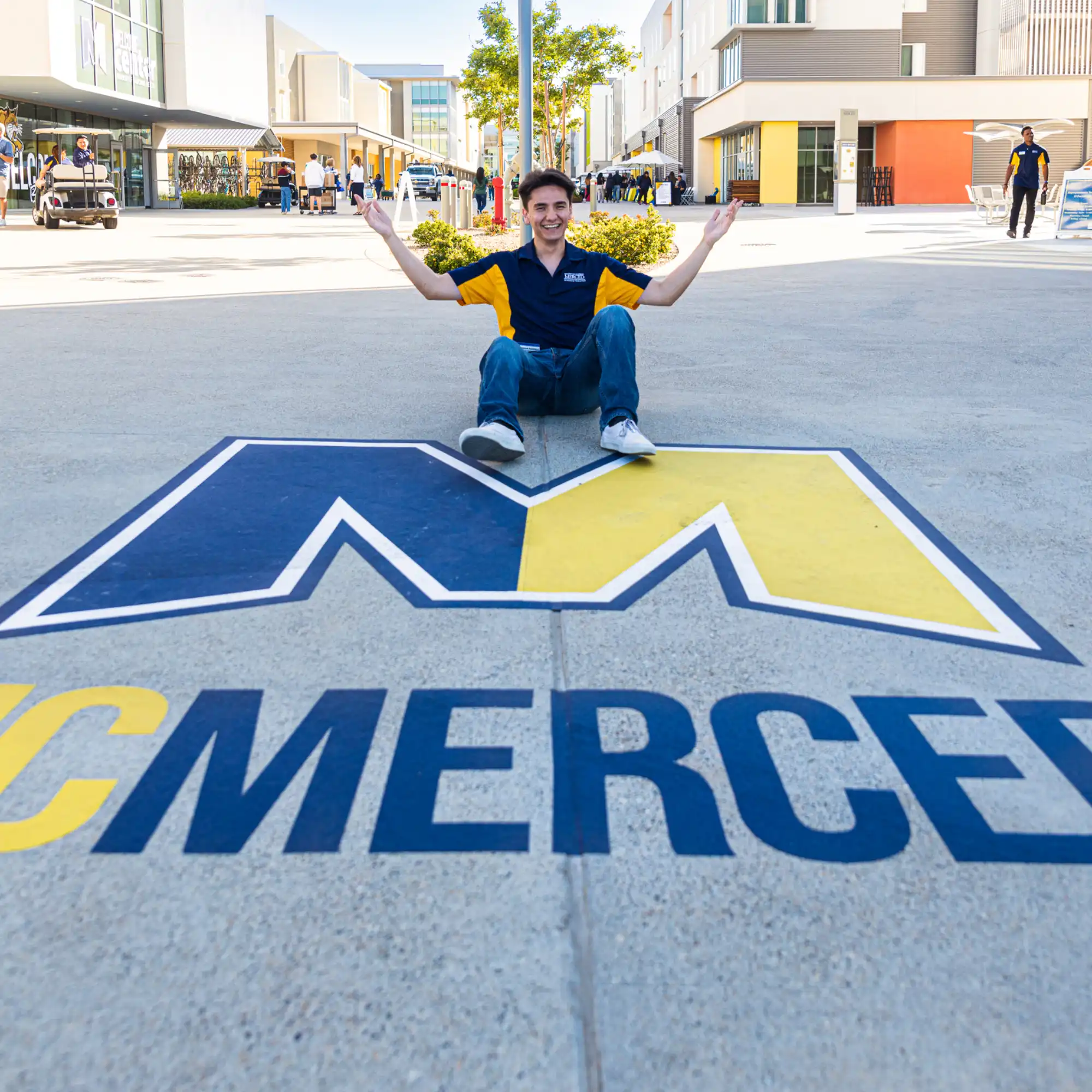 UC Merced student sitting behind the UC Merced logo on the academic walk.